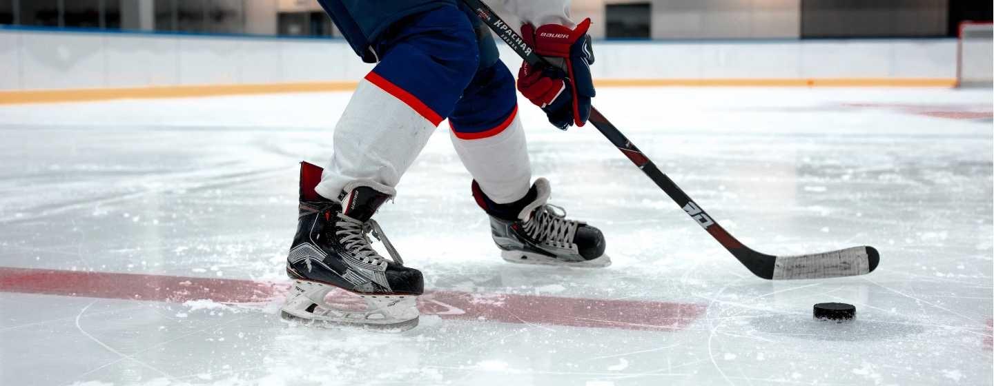 A hockey player skates on an ice rink, holding a hockey stick with a puck in the foreground