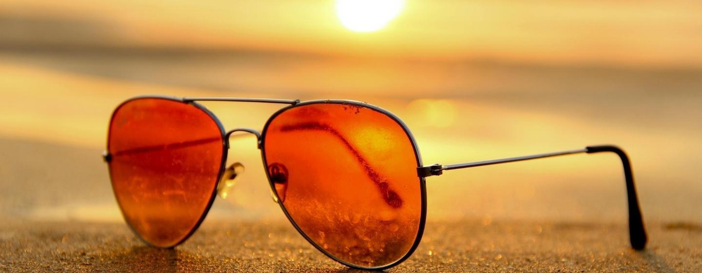 A pair of sunglasses on the shore with the sunset in the background.