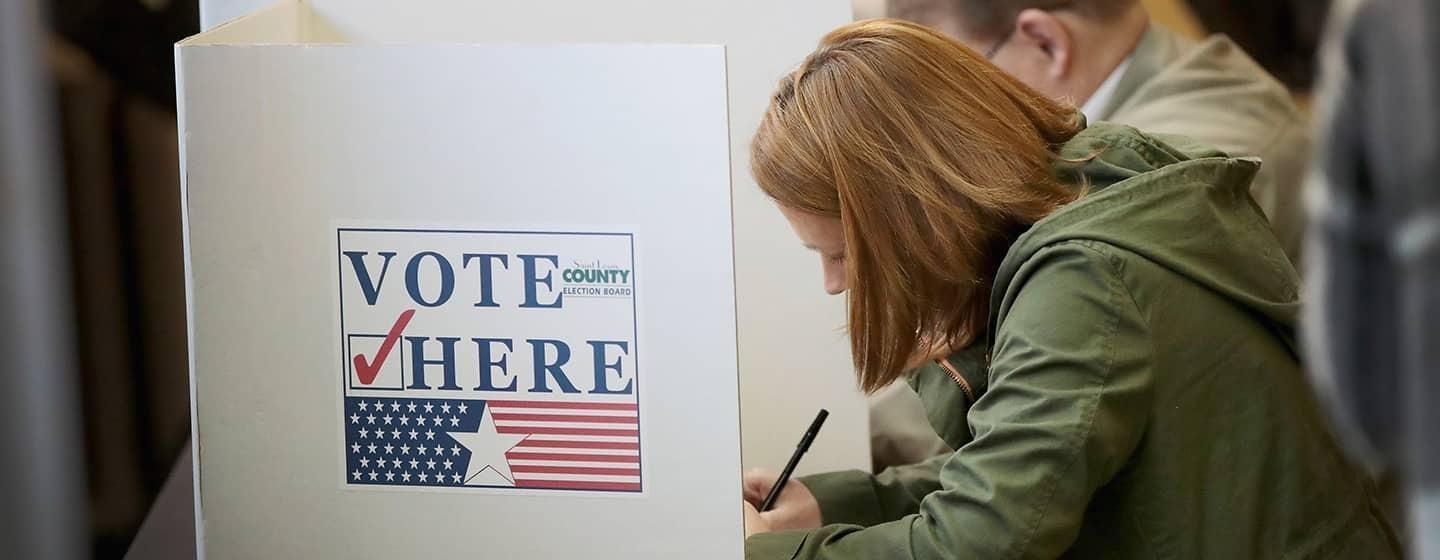 woman writing down on voting poll ballot with pen in line of voters