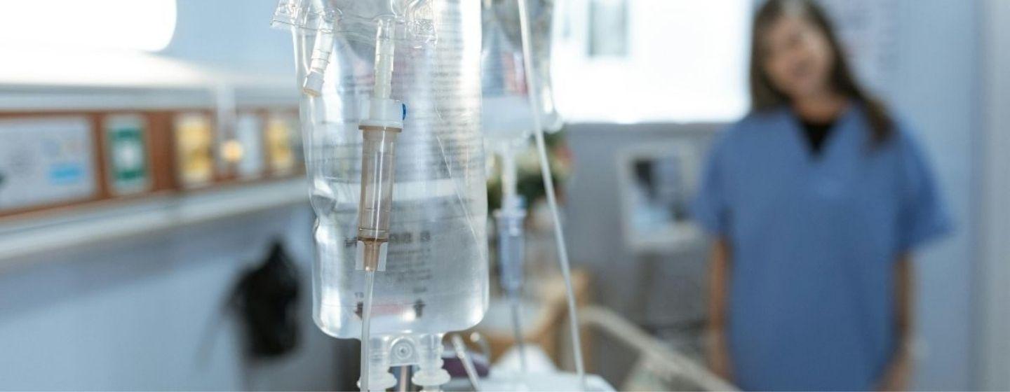 An IV bag, with a doctor blurred in the background.