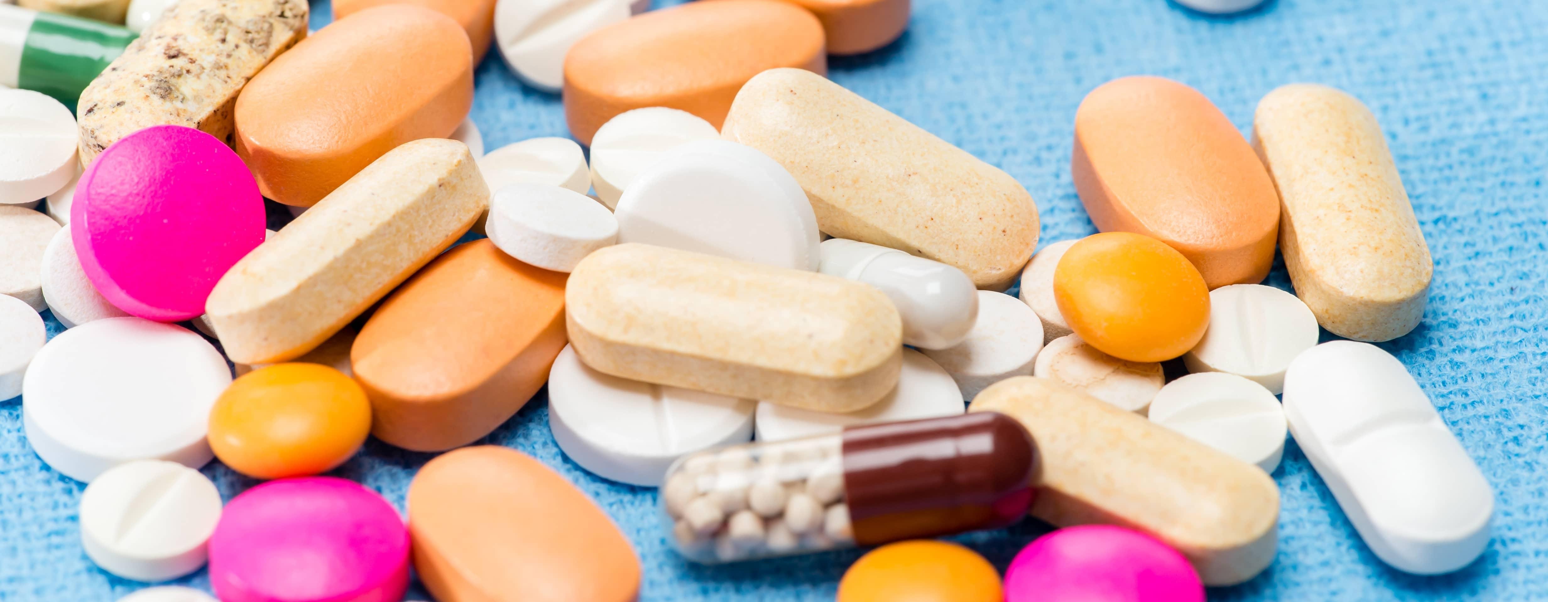 Multicolored and shaped pills and vitamins in a pile on a blue fabric background.