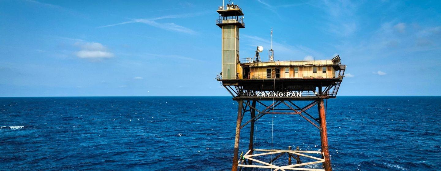 The Frying Pan Tower, a former U.S. Coast Guard light tower, in the middle of the ocean with clear blue skies.