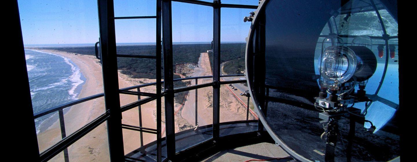 A view overlooking the beach and the road inside from the top of a lighthouse, looking out through the glass panels.