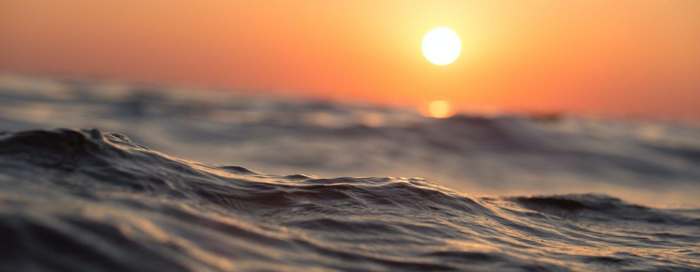 An ocean wave with a golden hour sunset in the background.