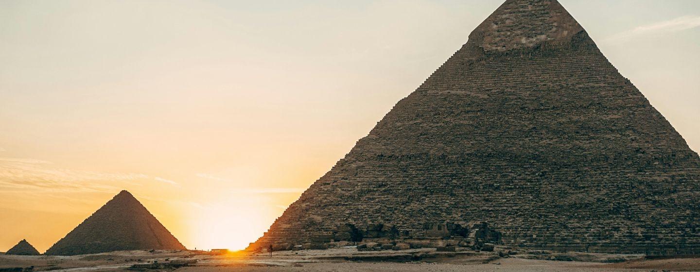 The pyramids in Egypt with the sun setting behind them.