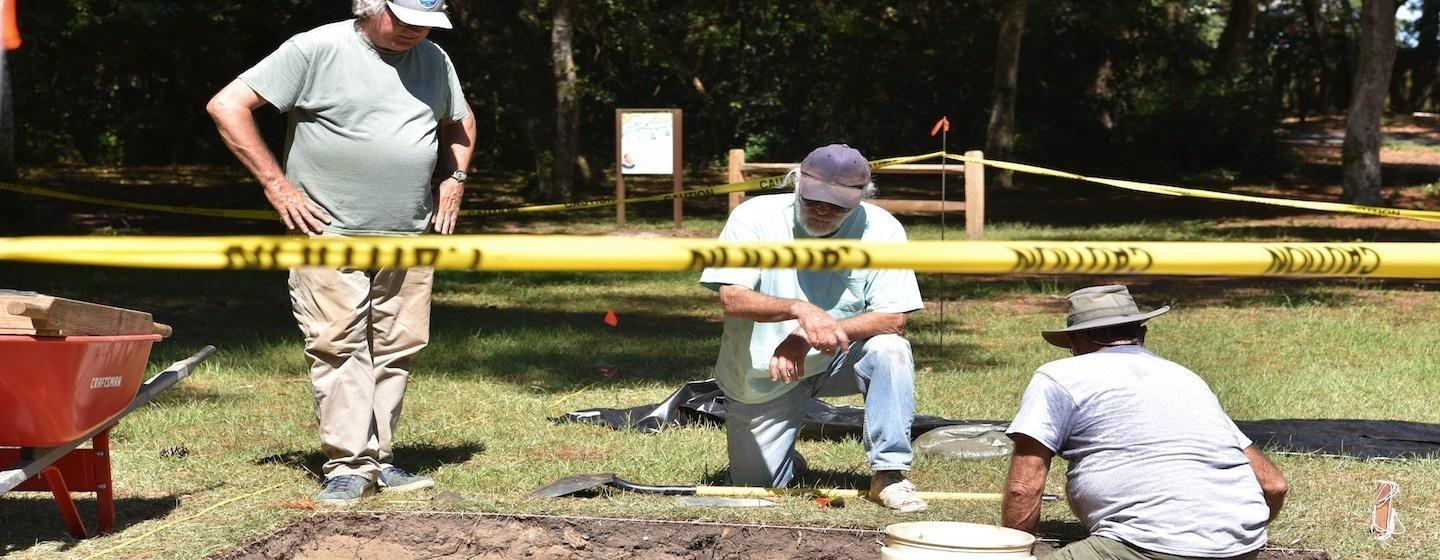 group of archaeologists digging behind caution tape