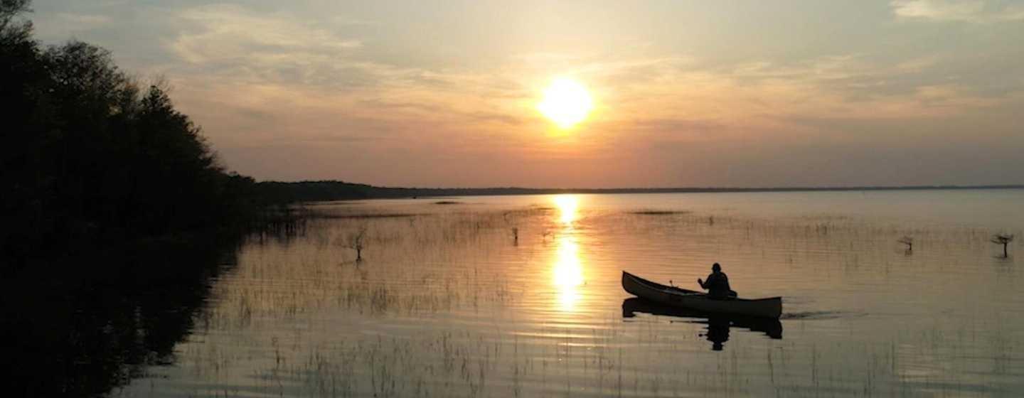 A lone canoe with a sole occupant rows through Lake Waccamaw at sunset