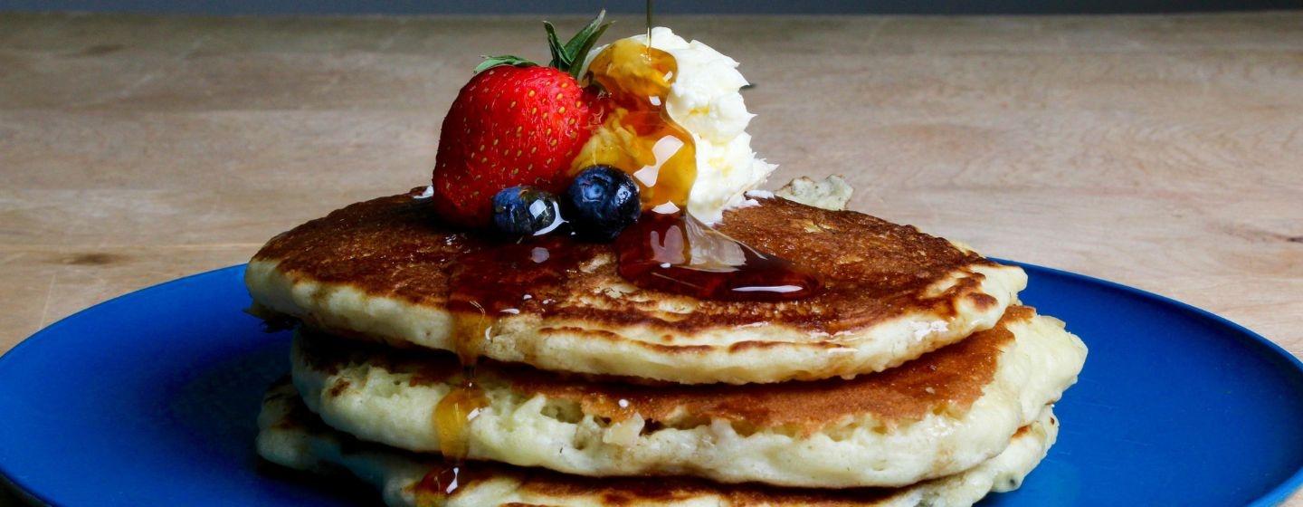 A stack of pancakes with fruit, butter and syrup on top.