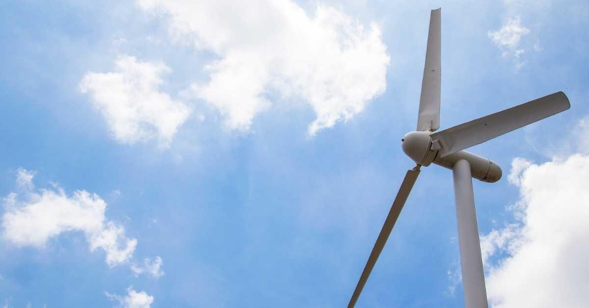 A wind turbine with a blue and cloud filled sky behind it.