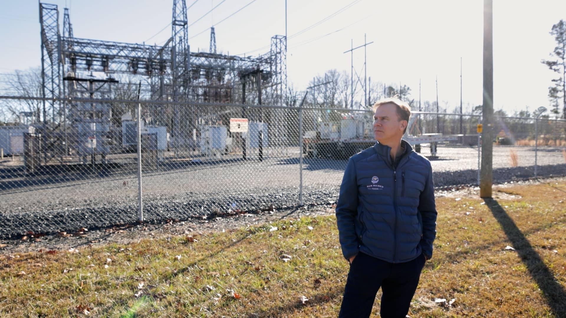 Joel Olsen stands in front of the substation in Biscoe, NC. Power generated at his farm flows down transmission lines to this substation to fill the energy needs of Biscoe and beyond.