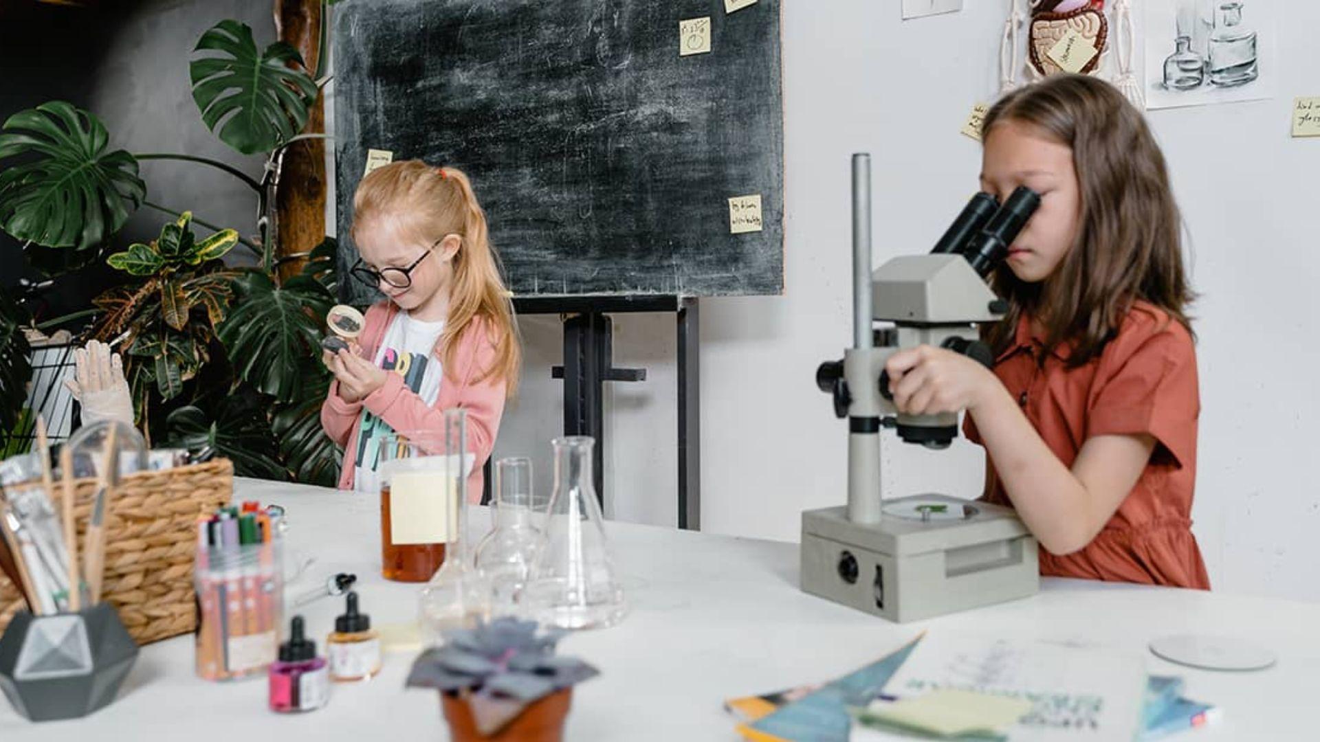 Two girls in a science classroom doing various tasks.
