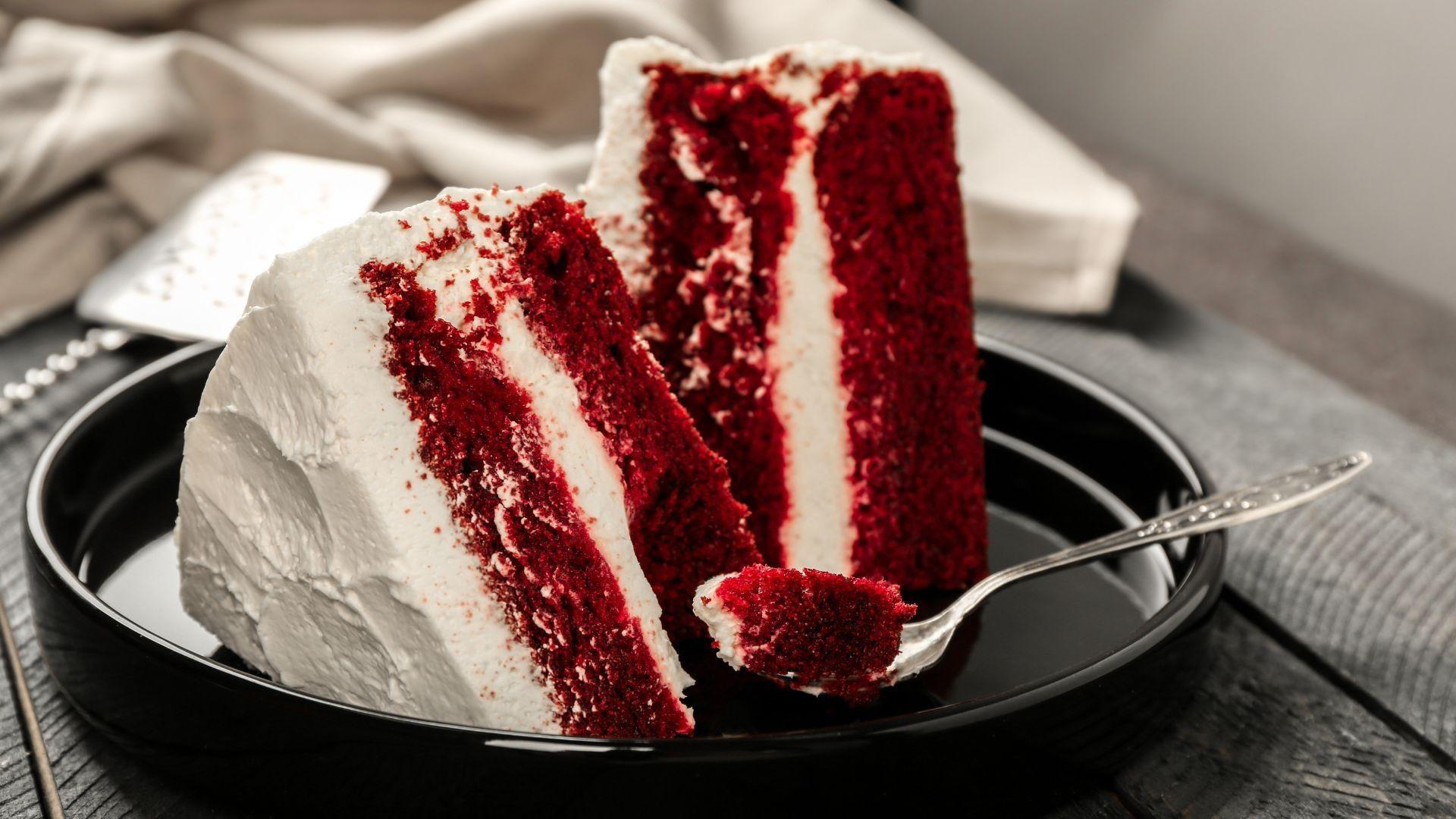 Two slices of red velvet cake with white frosting on a black plate.