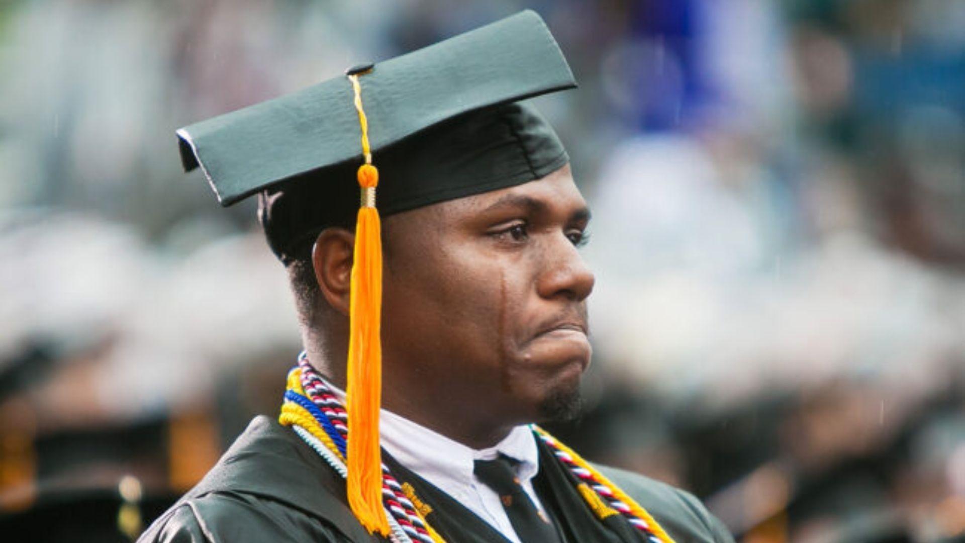 A Black man in a graduation cap crying.