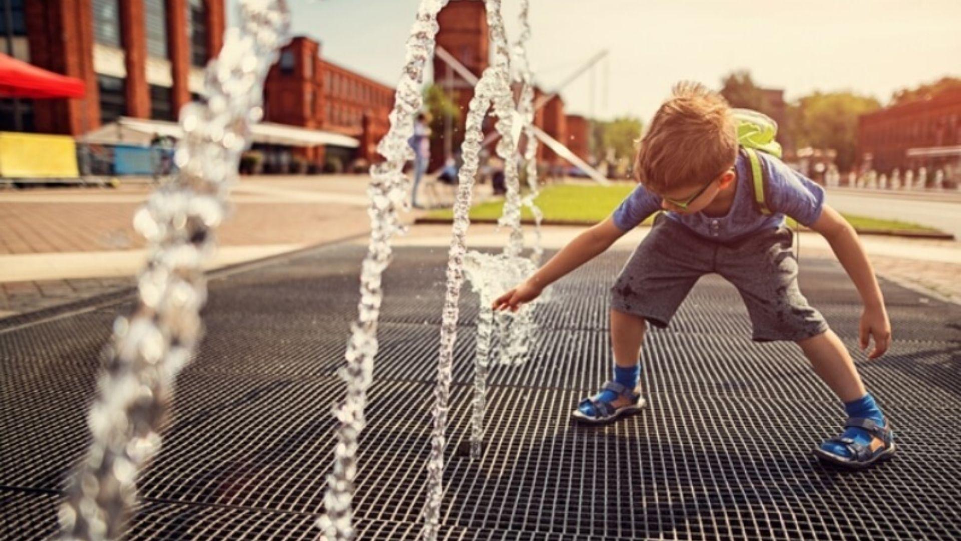 A young child playing in a park sprinkler.