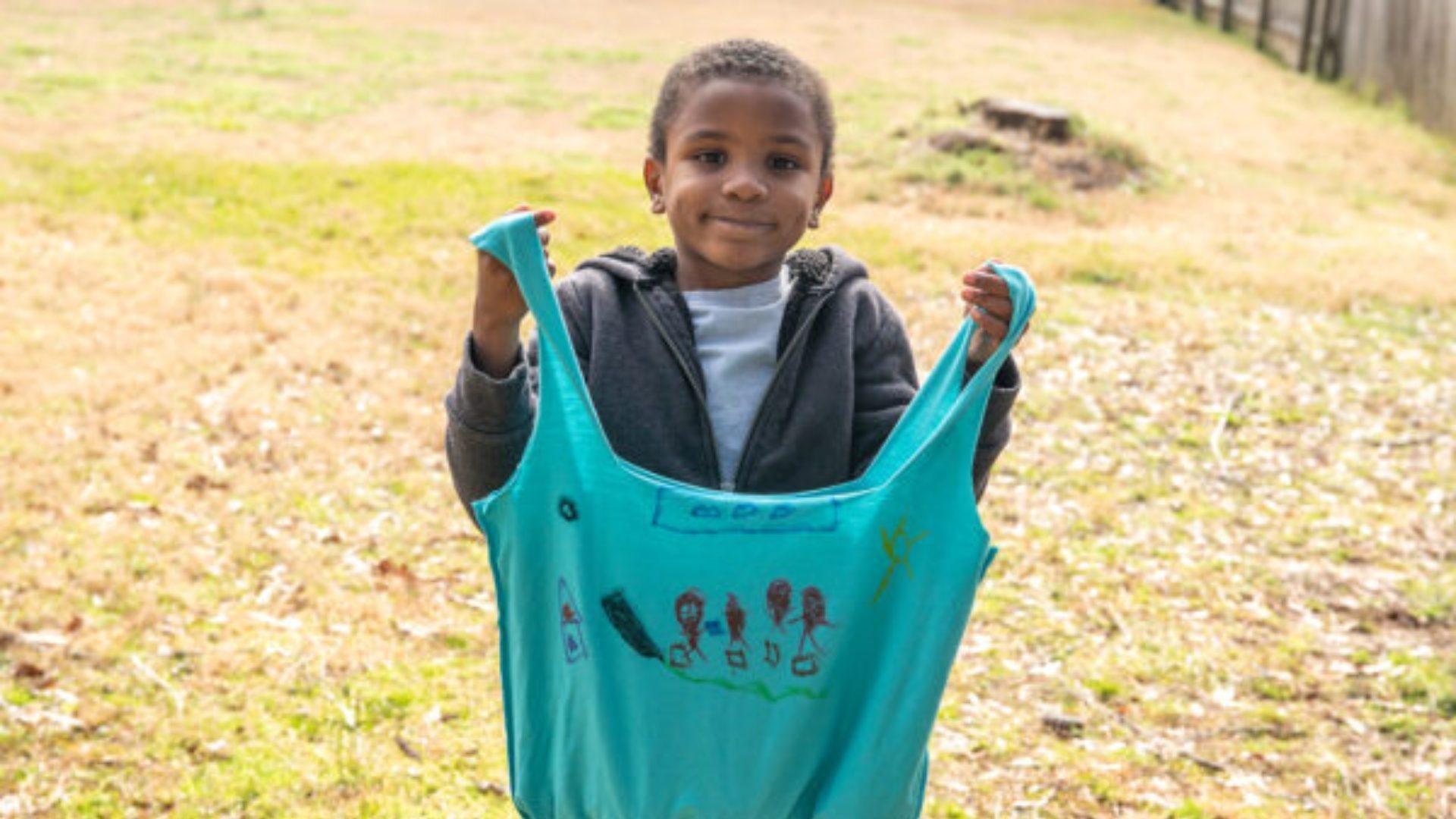 A black boy holding a blue bag made out of a recycled tee shirt.