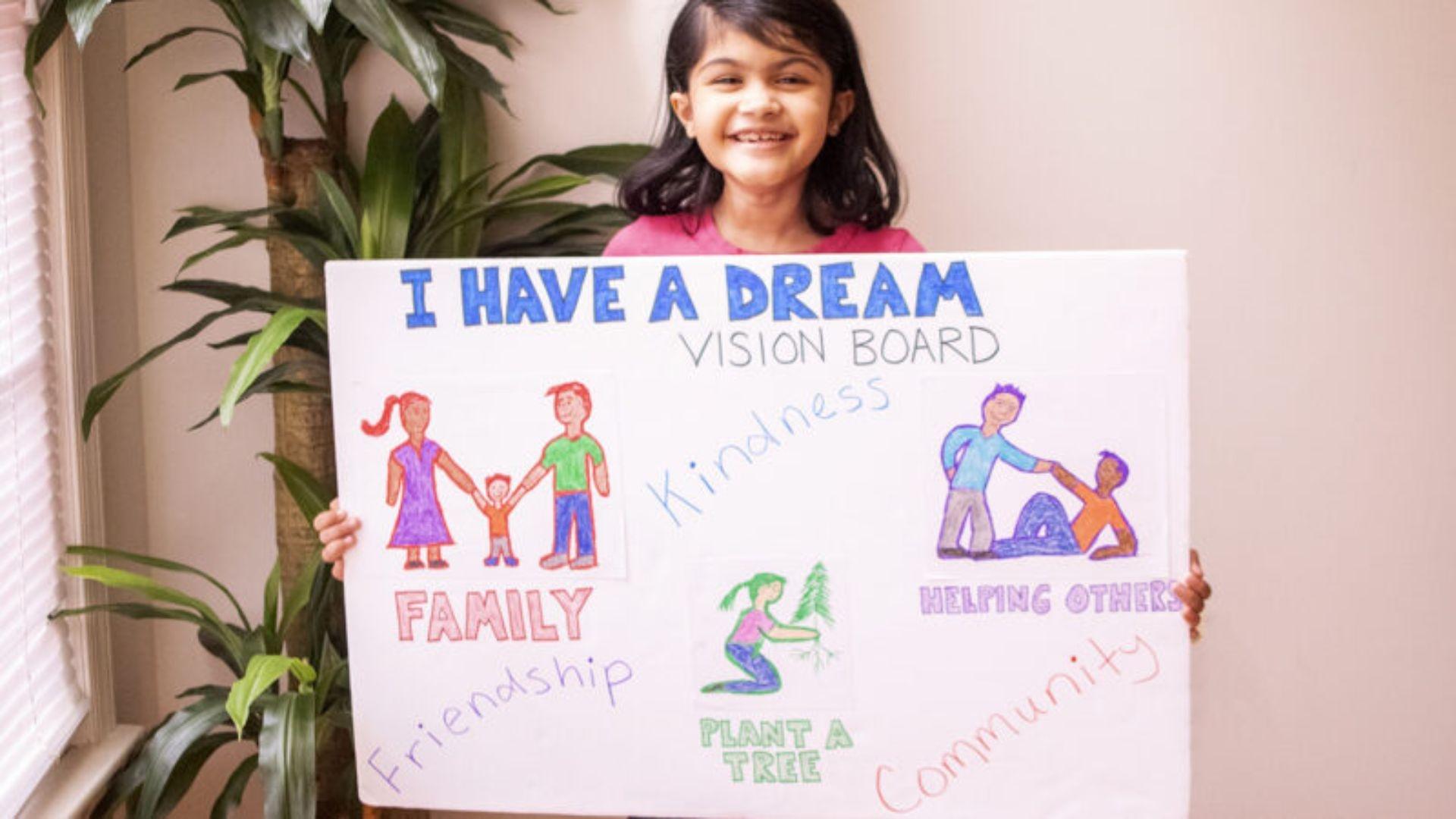 A girl holding up her "I Have A Dream" vision board while smiling.
