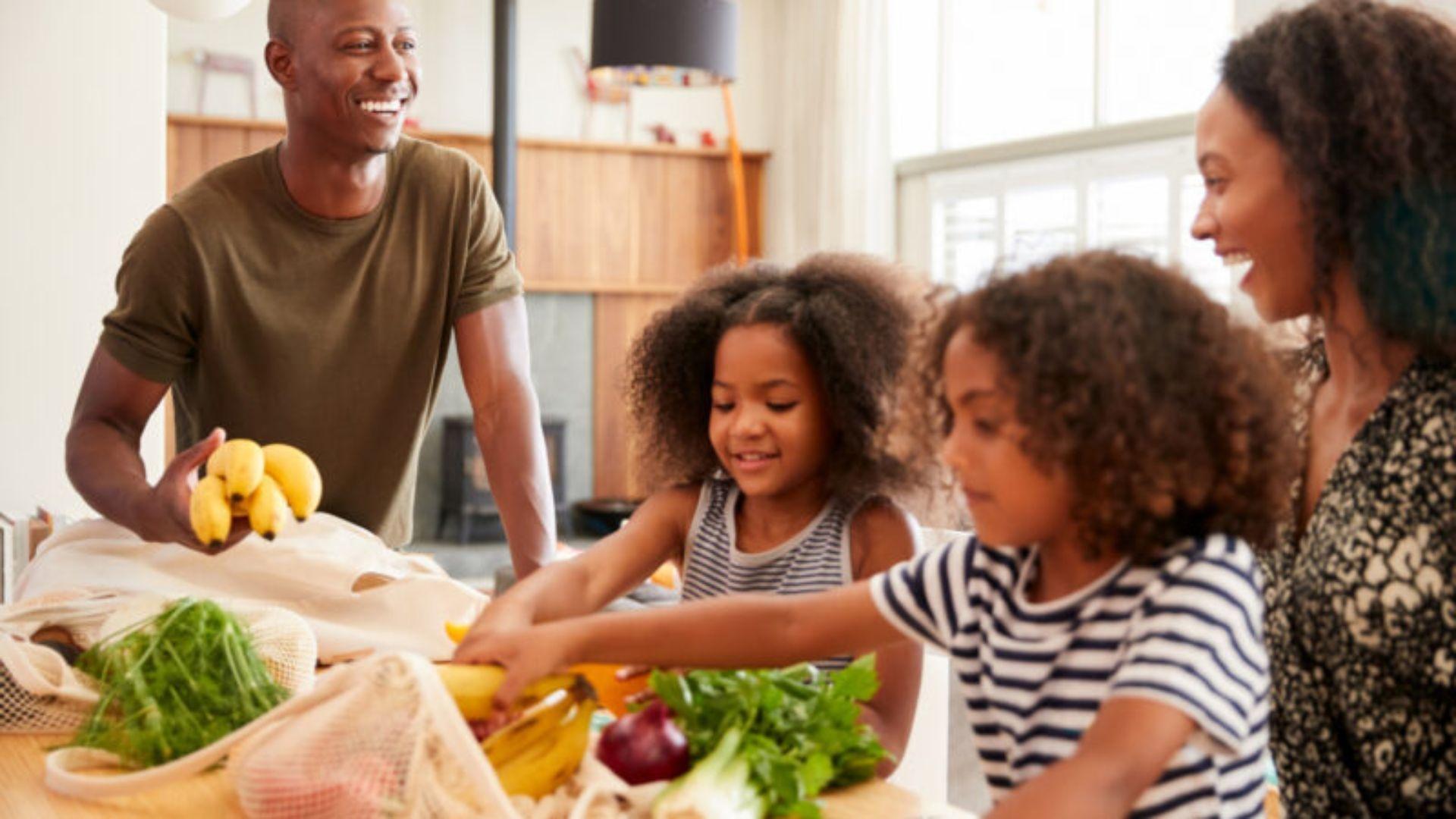 A family of four put away vegetables and fruit groceries.