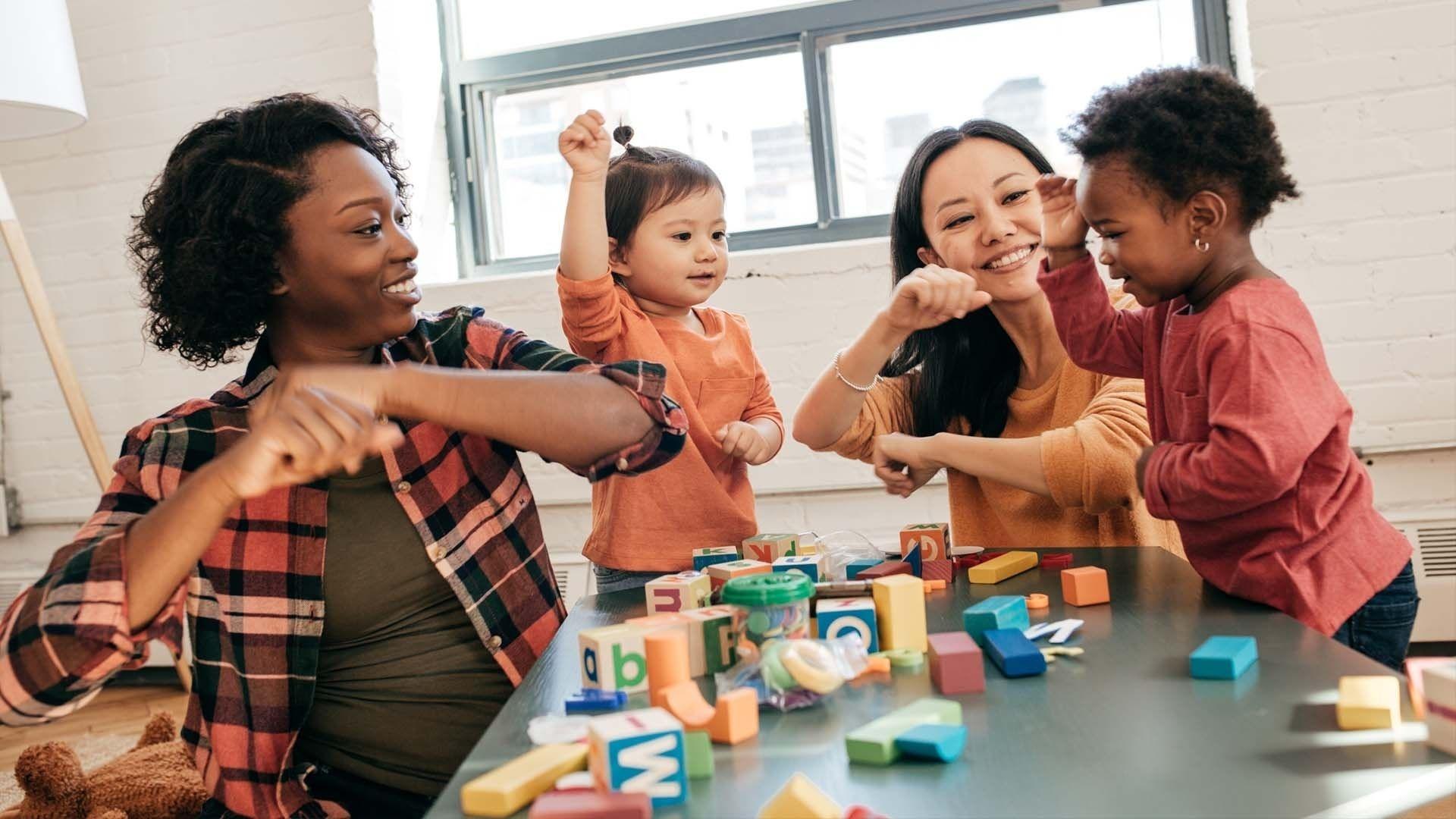 Two moms and their two children play with blocks at a table.