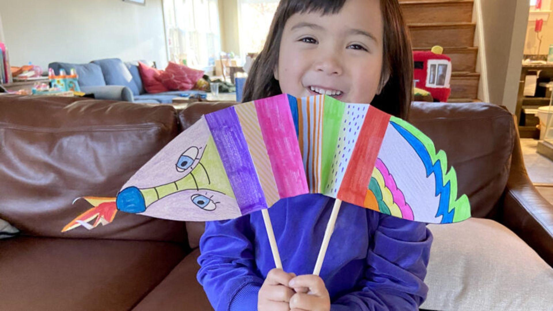 A child holding up a colorful paper dragon they made.