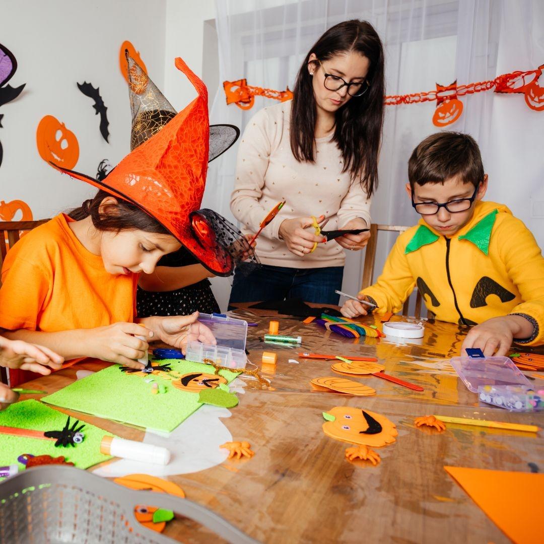 Two children and their parent dressed for halloween doing halloween themed crafts at a dining room table.