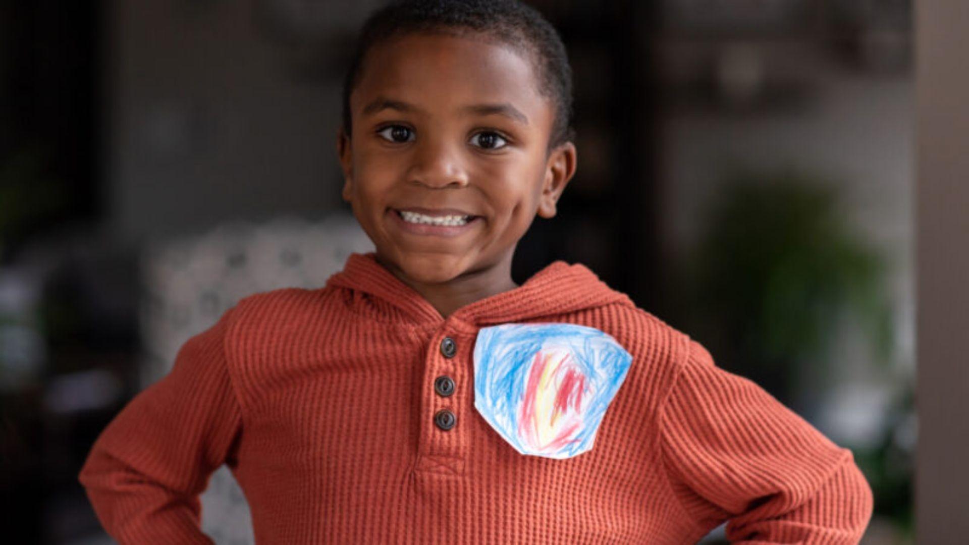 A Black boy smiling and wearing a craft as a pin on his shirt.