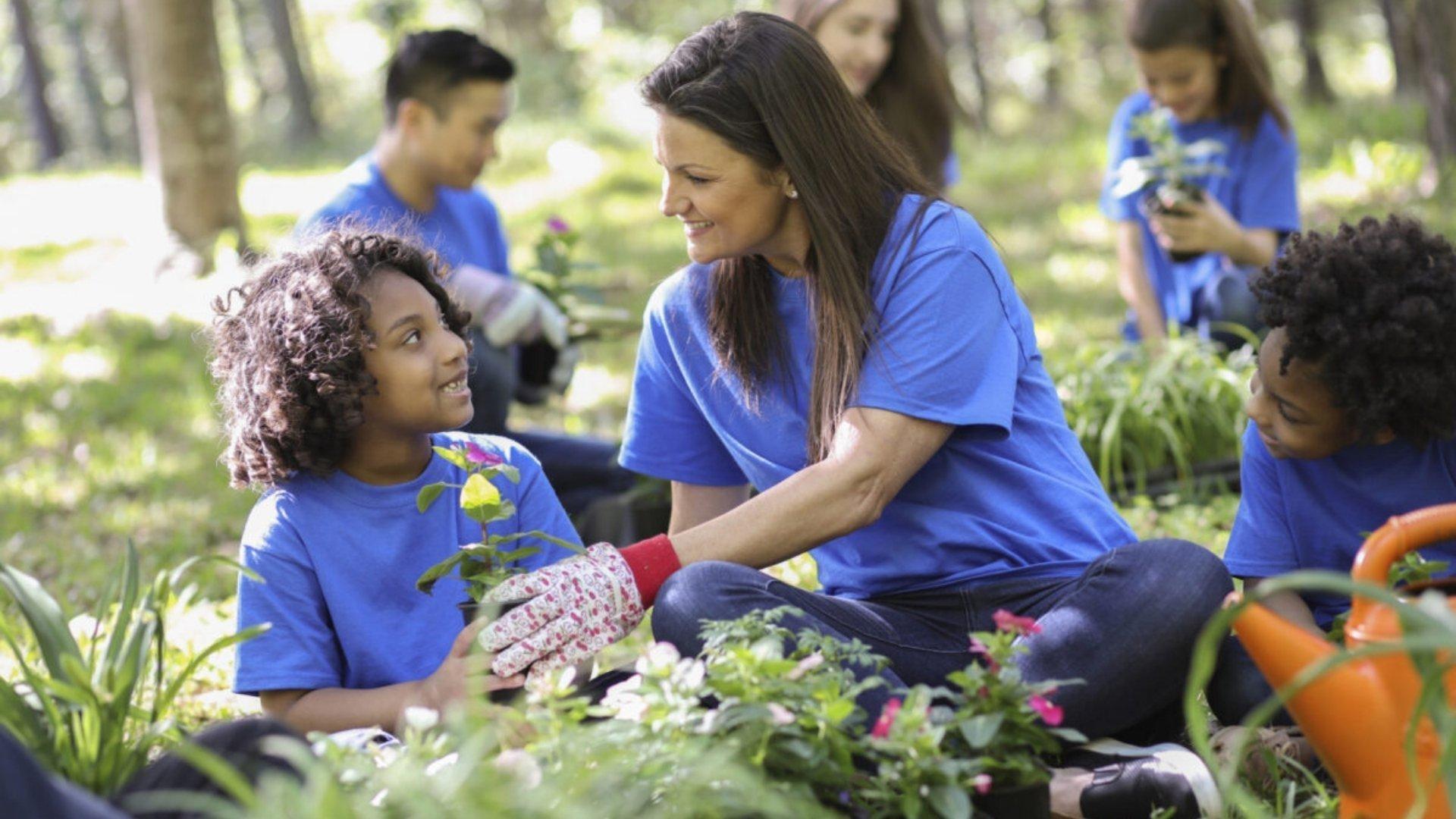 Children and guardians in blue tee shirts planting outside.