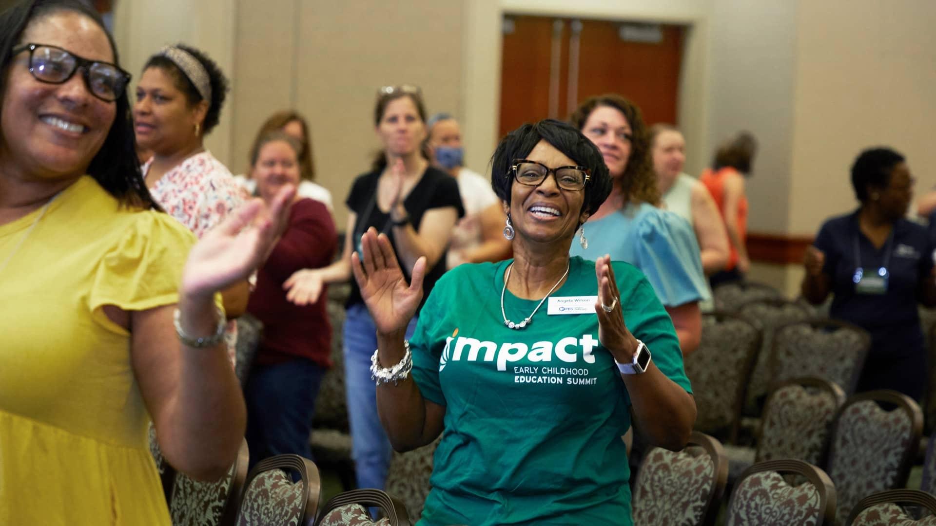 Attendees at the 2022 Impact Summit stand in the ballroom during the opening session
