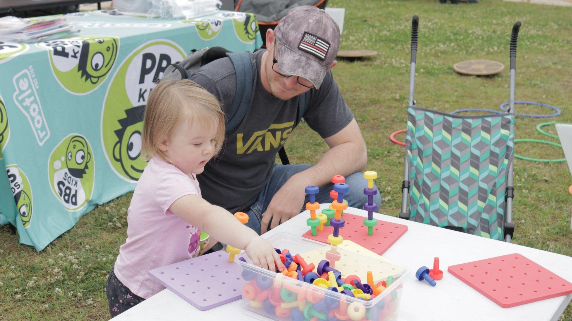 A father and daughter play with stacking pins at a Rootle Roadster Tour stop.