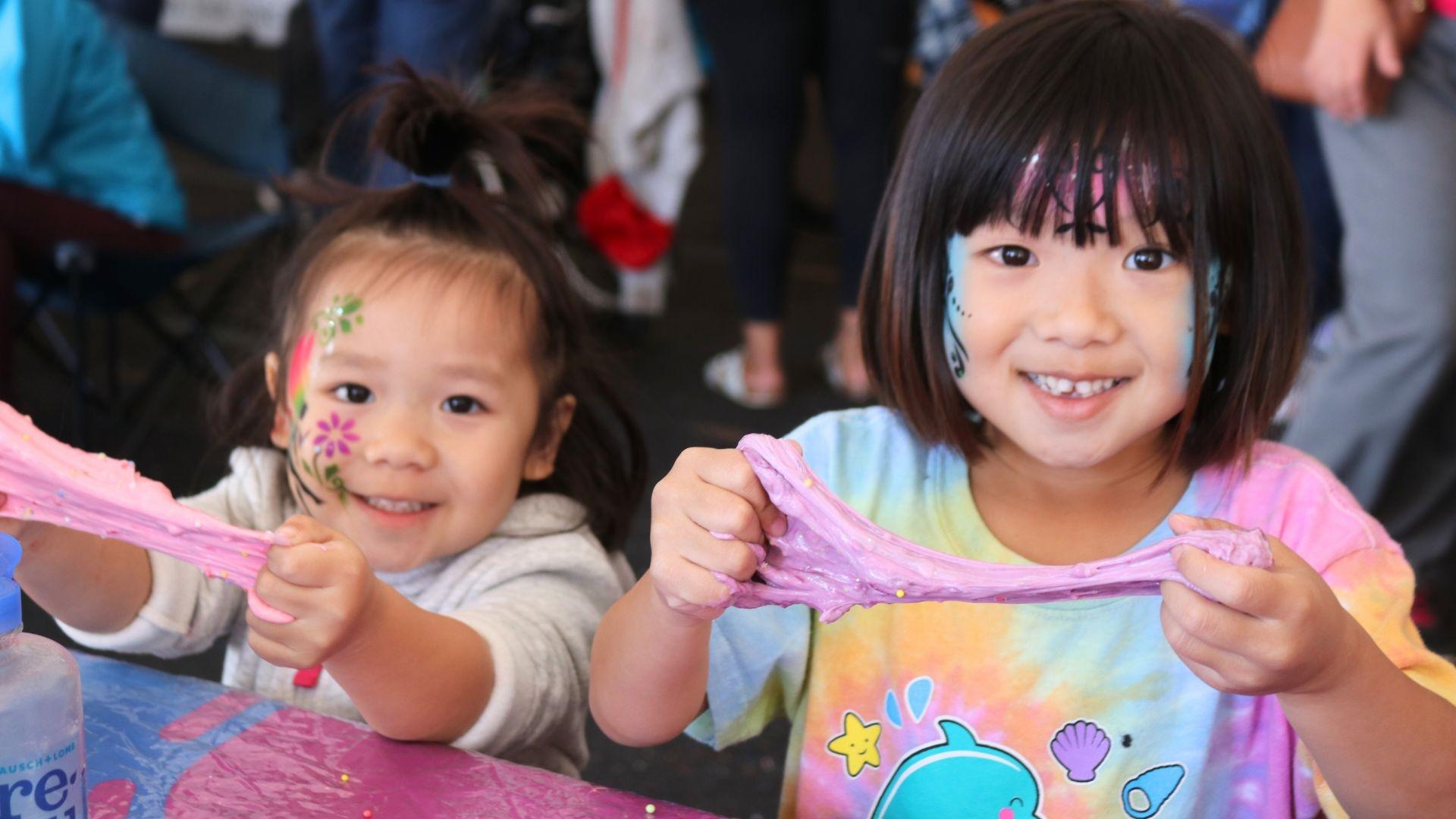 Sisters who have their faces painted play with slime at a Rootle Roadster Tour stop.
