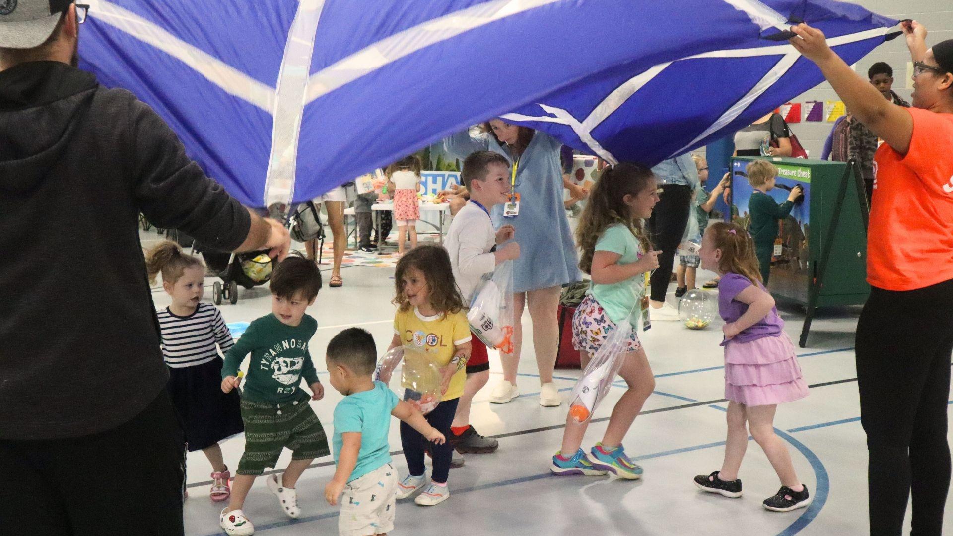 Kids run around under a parachute at a Rootle Roadster Tour stop.