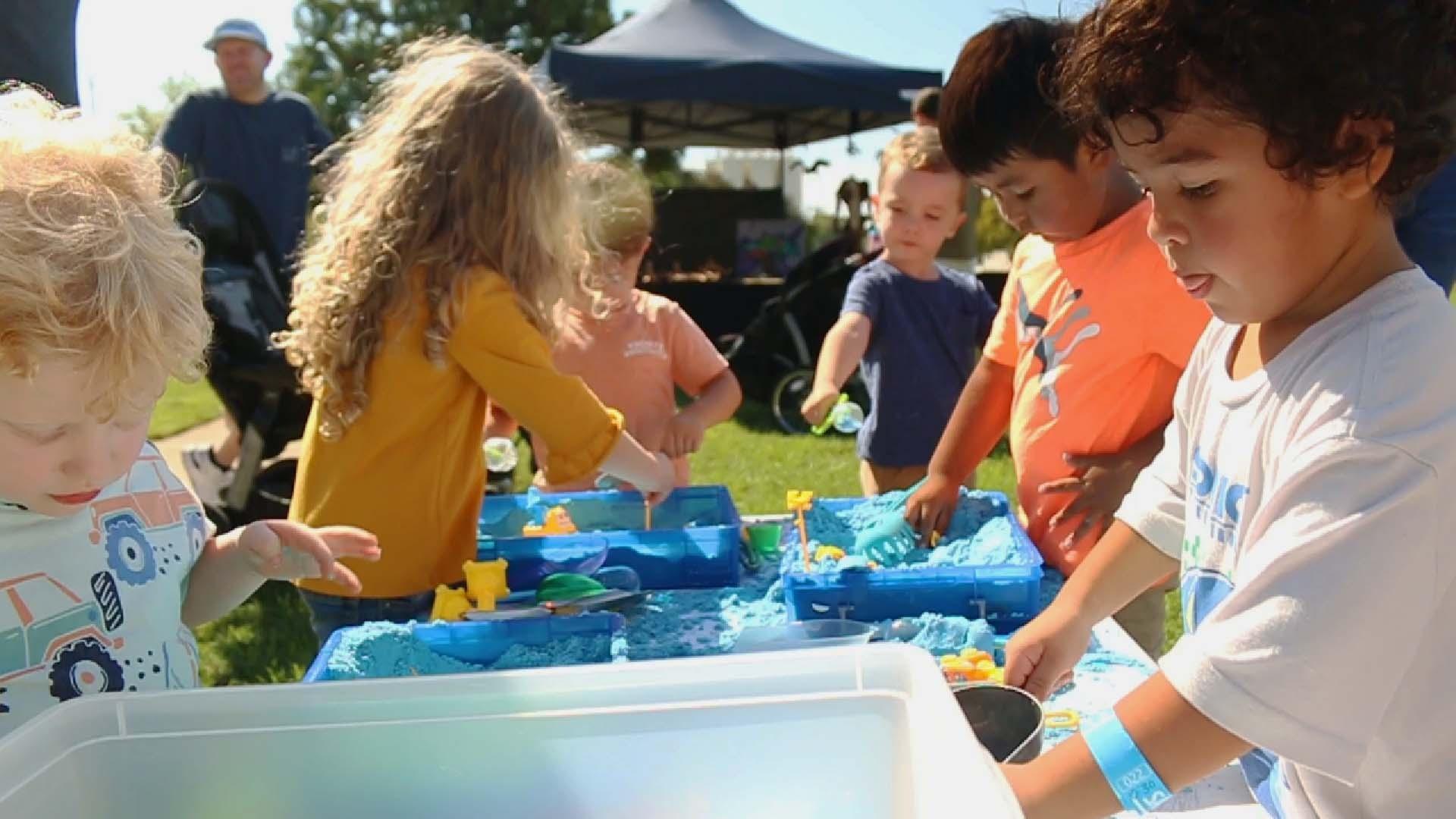 Young children gather around buckets of kinetic sand with toys in them at a Rootle Roadster Tour stop.