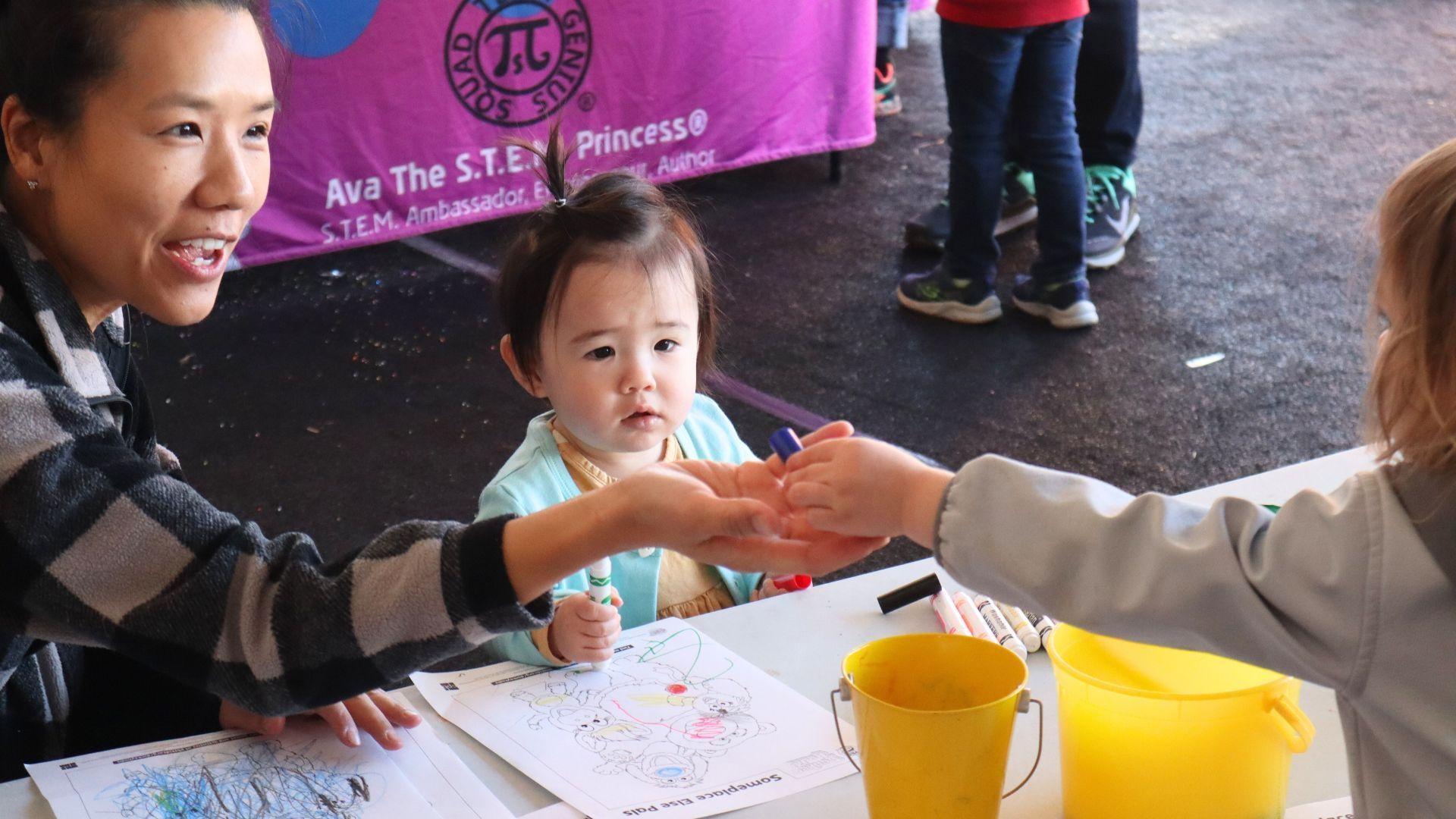 A kid shares with a baby and their mom at a Rootle Roadster Tour stop.