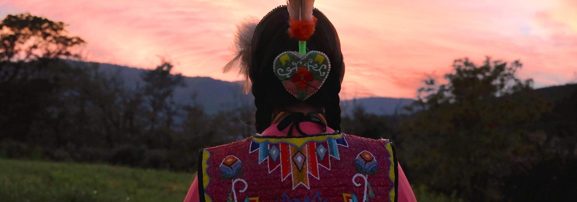 Angelina Jumper Huckleberry faced away in beaded dress with a sunset behind her.