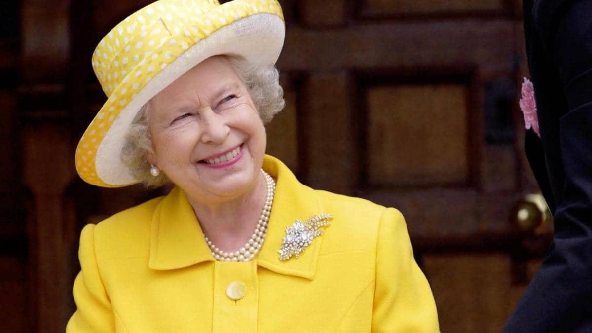 Queen Elizabeth II smiling, wearing a yellow suit and yellow and white hat