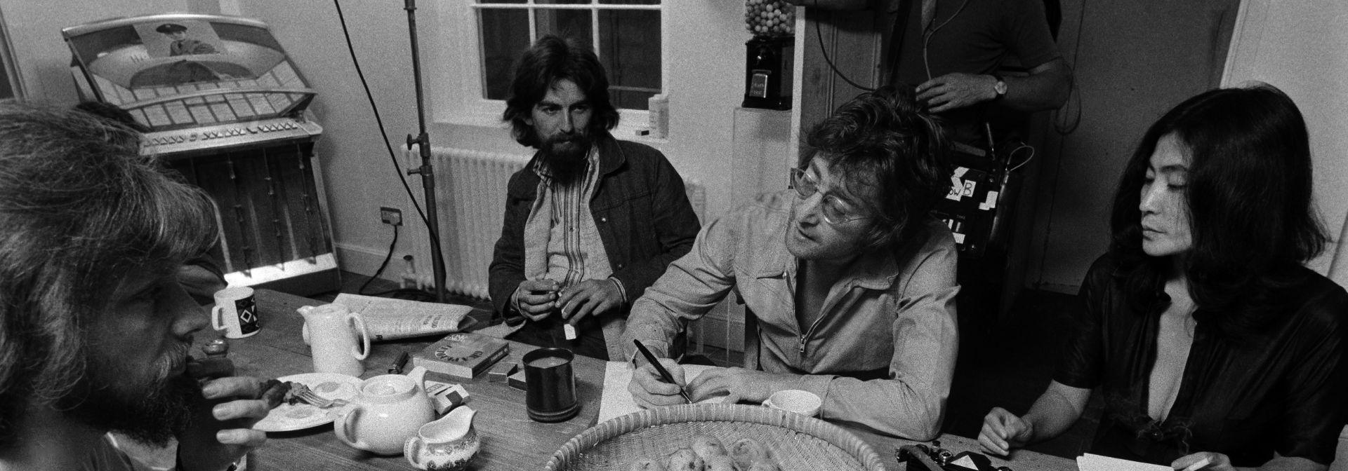 George Harrison, John Lennon and Yoko Ono sitting around a table.