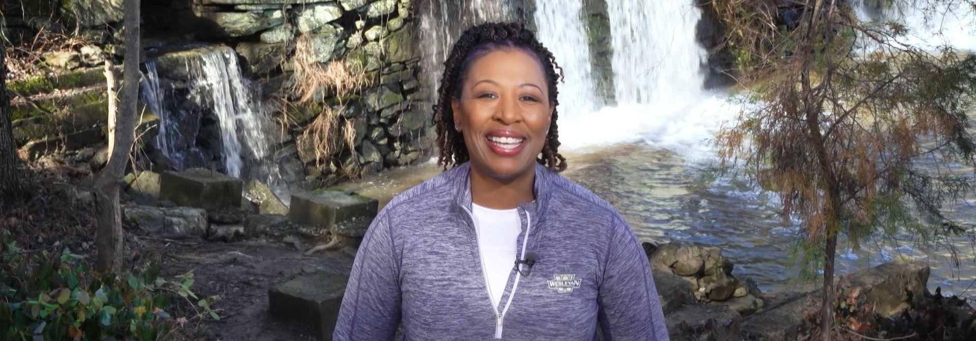 Deb Holt Noel standing in front of a rocky waterfall at a NC state park and smiling at the camera