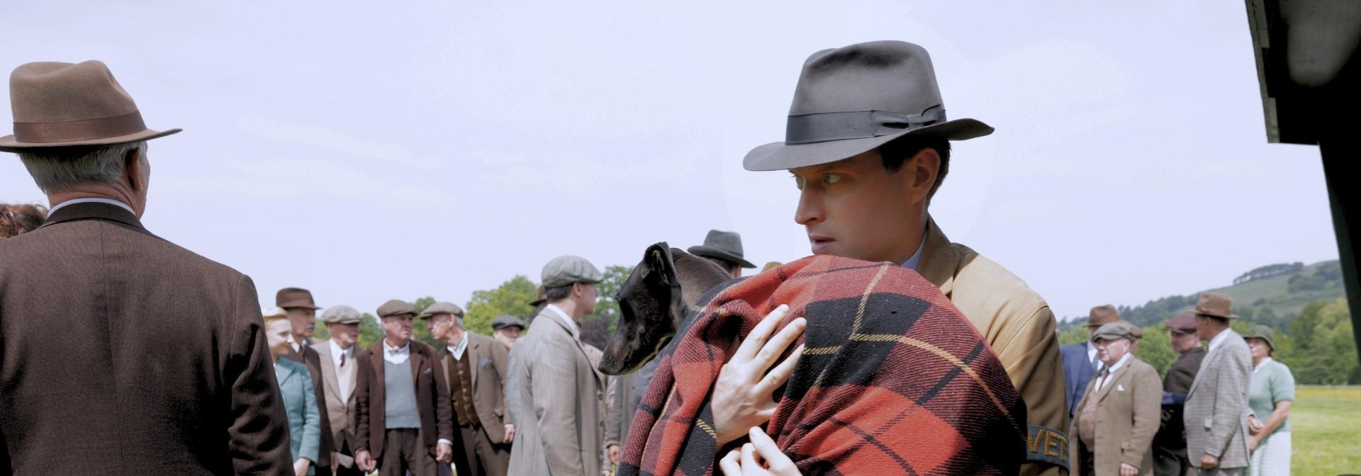 James Herriot (Nicholas Ralph) holding a greyhound wrapped in a flannel blanket.