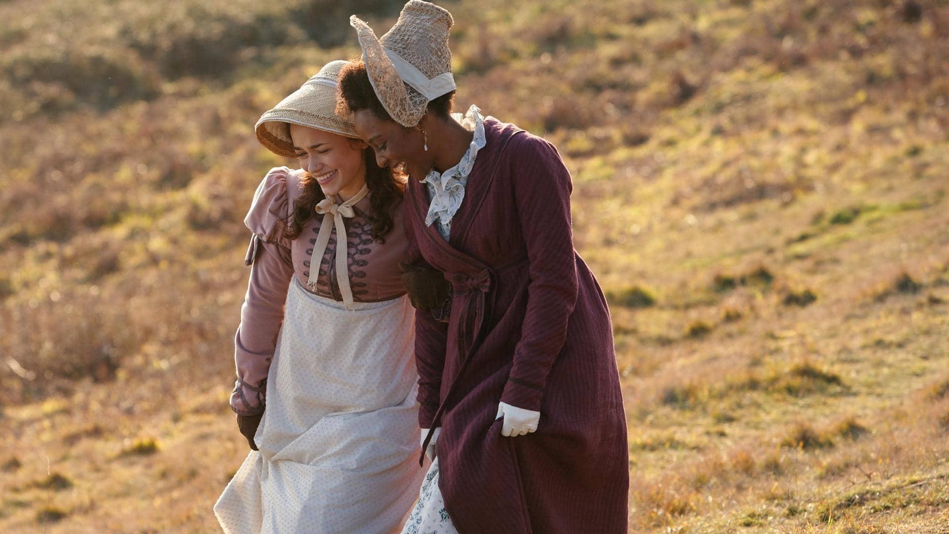 The leads of Sanditon, two woman wearing Regency era fashions walk in a field