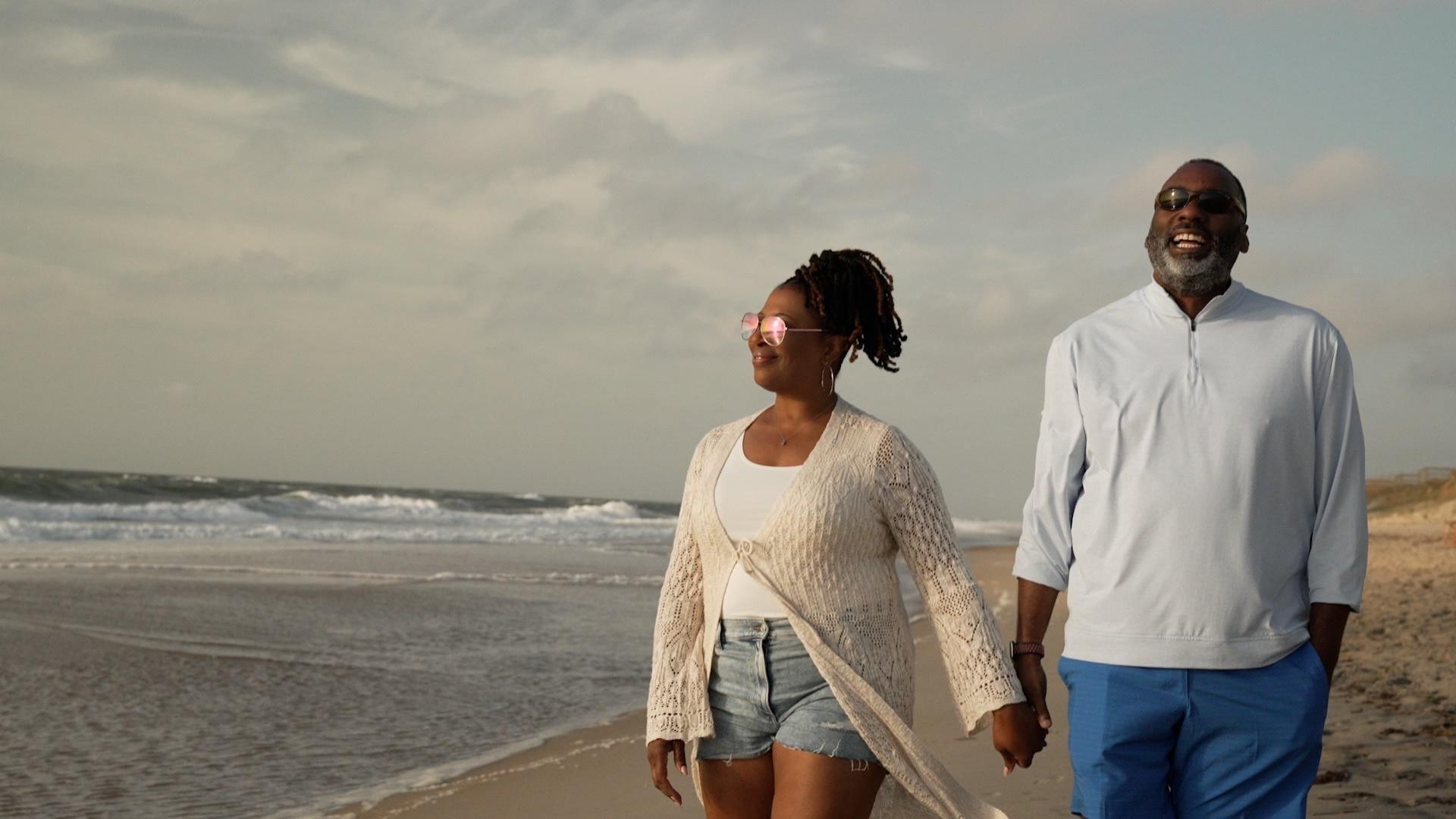 Host of NC Weekend Deborah Holt Noel with her husband holding hands while walking on an NC beach.