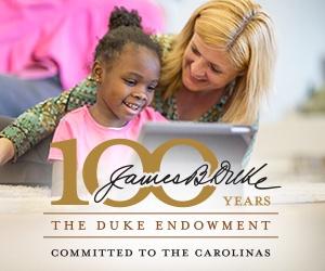A white woman looks over the shoulder of a black child who is on a computer with the James B. Duke 100 Years logo for The Duke Endowment.