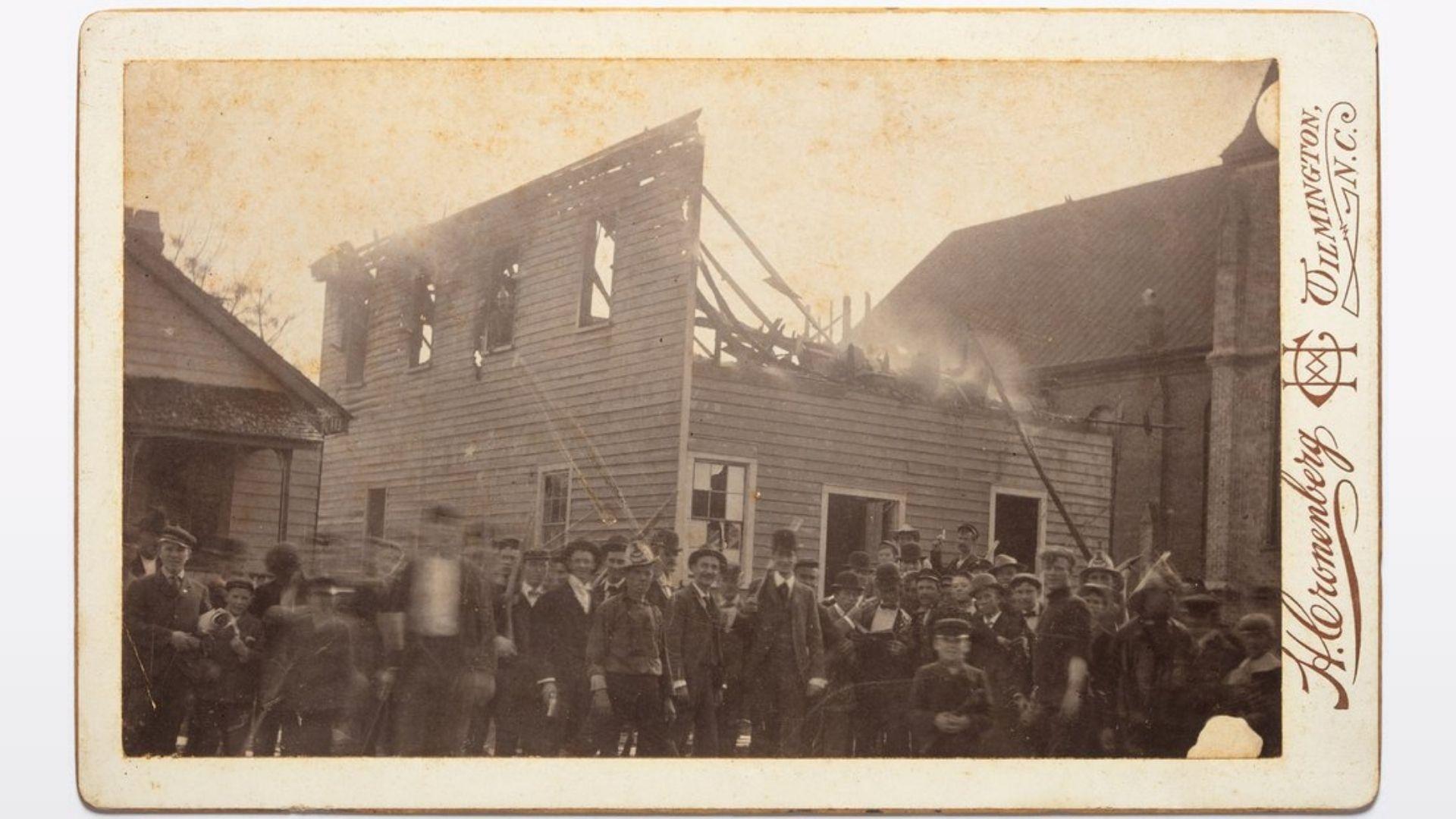 A mob celebrates in front of the burned Love & Charity Hall which housed the black-owned and -edited newspaper, The Daily Record. Courtesy of New Hanover County Public Library.