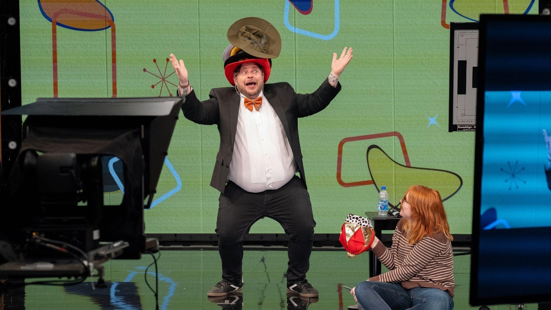 It’s tough to wear so many hats! Mr. Garin shows off his balancing skills as producer Izzy Daniels-Connor passes him the next challenge.