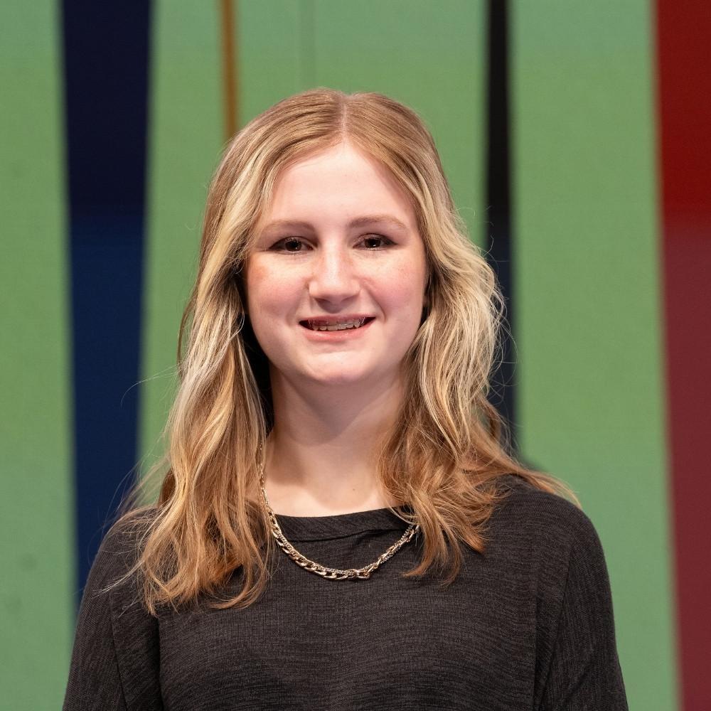 Lily, ninth grader, a young white girl with long blonde hair wearing a black heathered shirt and a golden chair necklace.