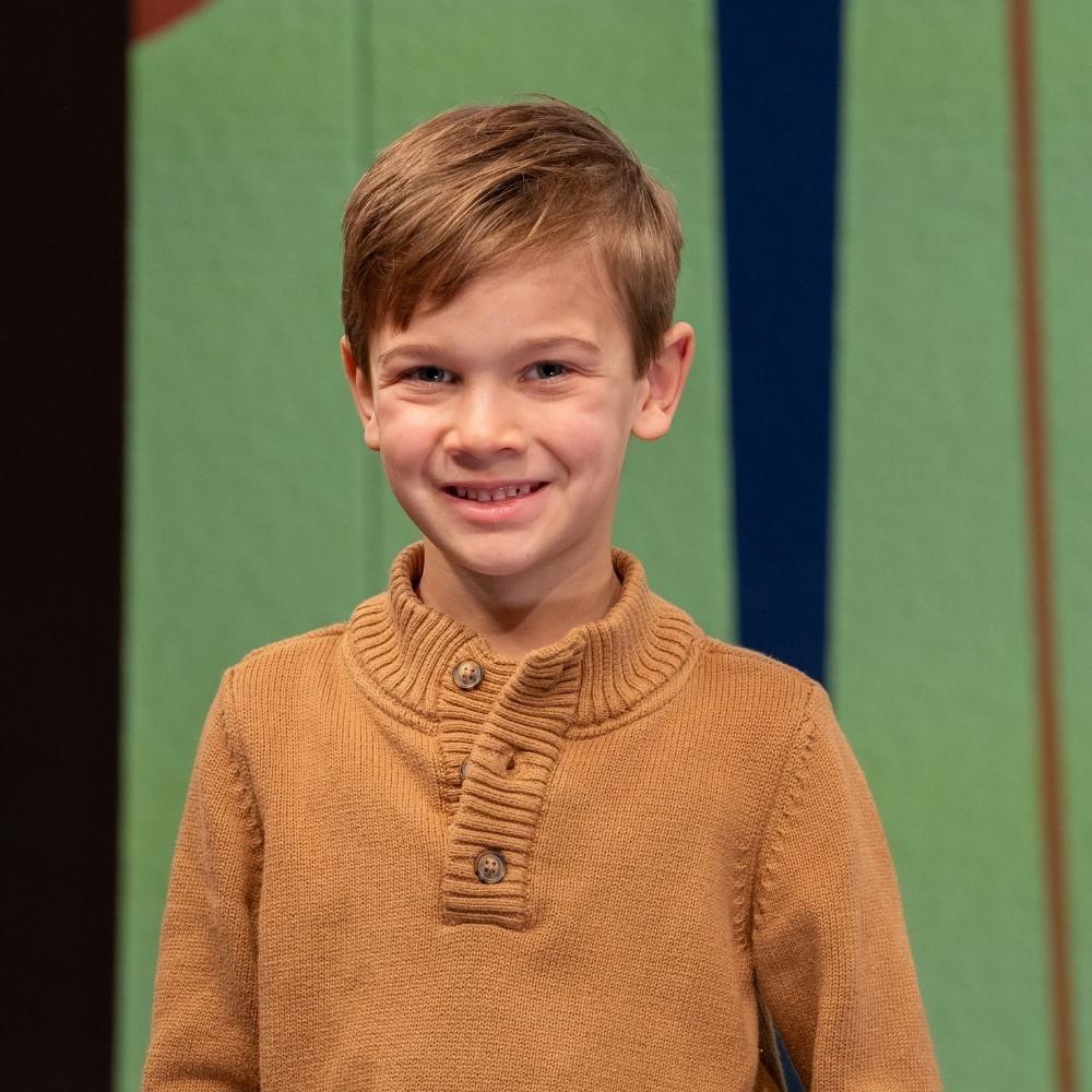 Connor, first grader. A white boy with a blonde combover and wearing a quarter-buttoned, orange sweater.