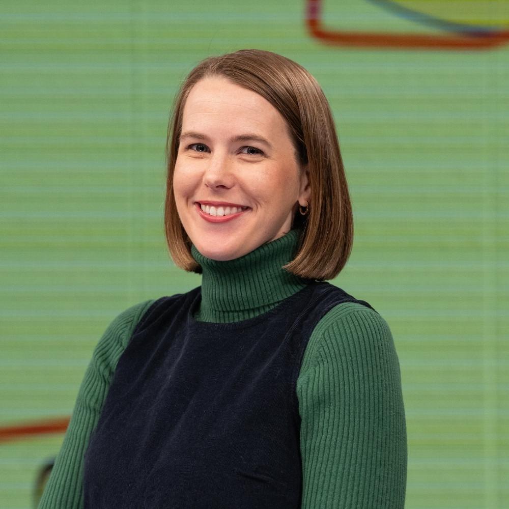 Dr. Emily Herring, Public Health Veterinarian. A white woman with a brown bob haircut, wearing a black vest over a green turtleneck.