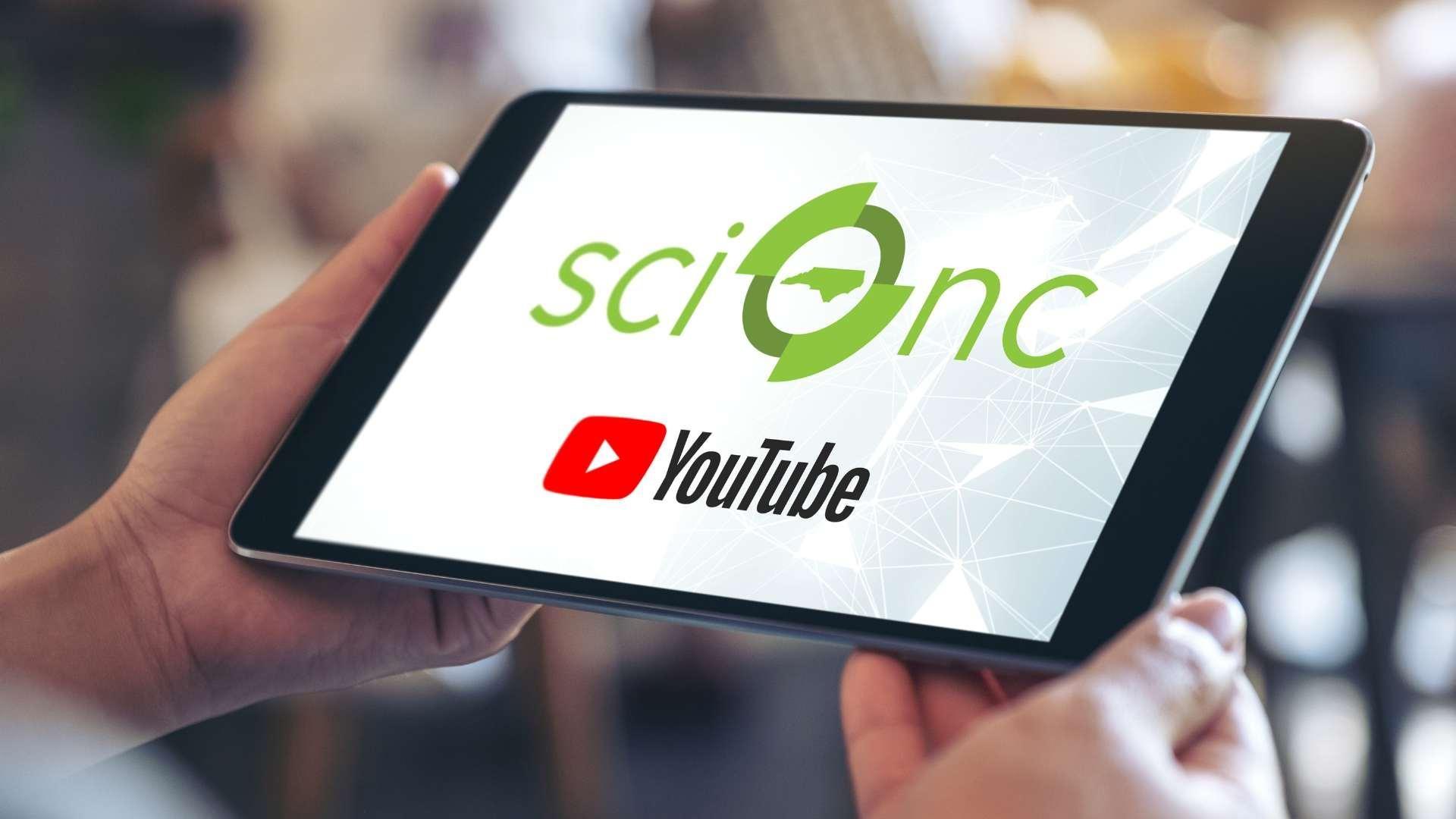 Hands holding an iPad with a screen featuring the Sci NC and YouTube logo.