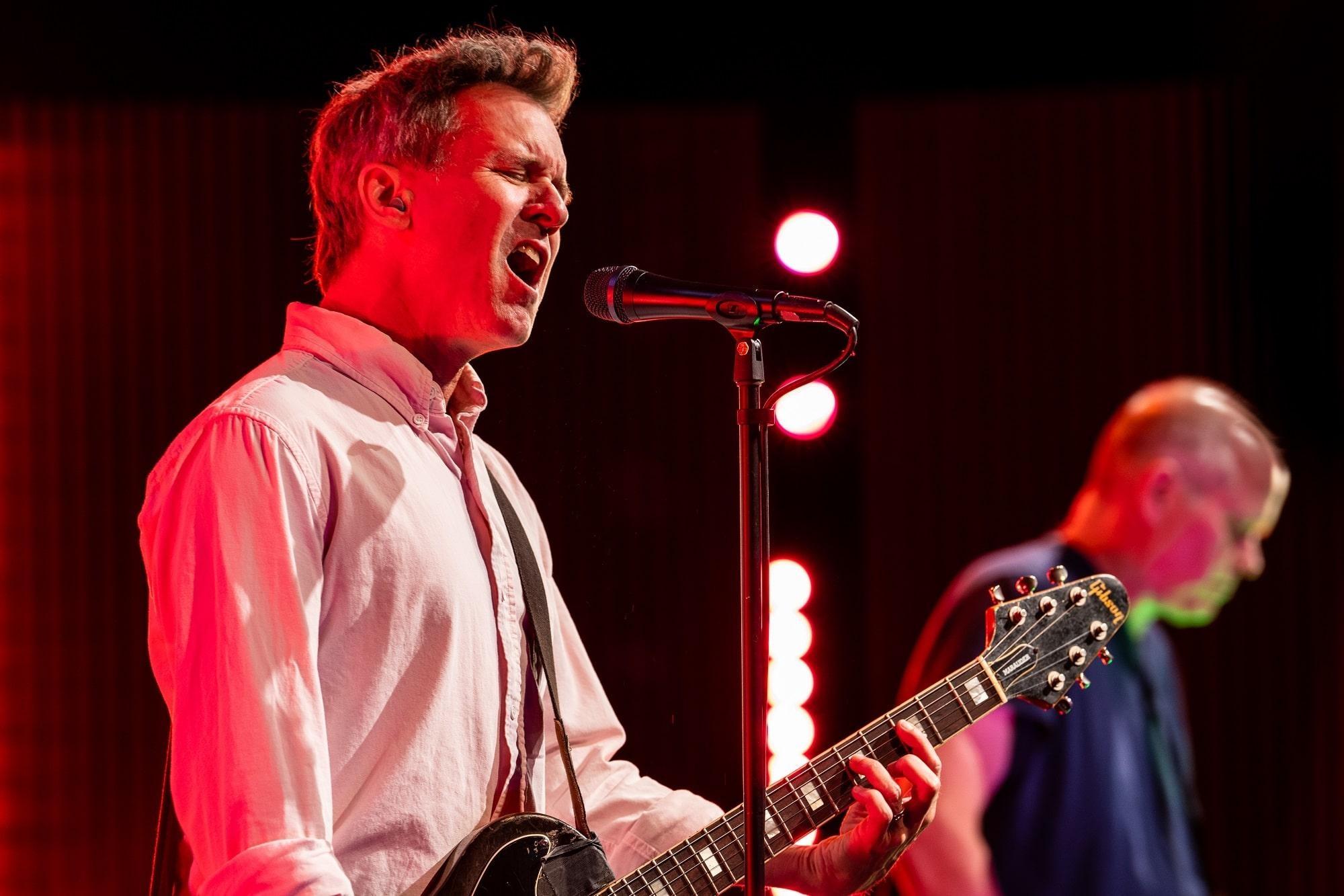 Mac McCaughan of the band Superchunk plays guitar while singing into a mic.