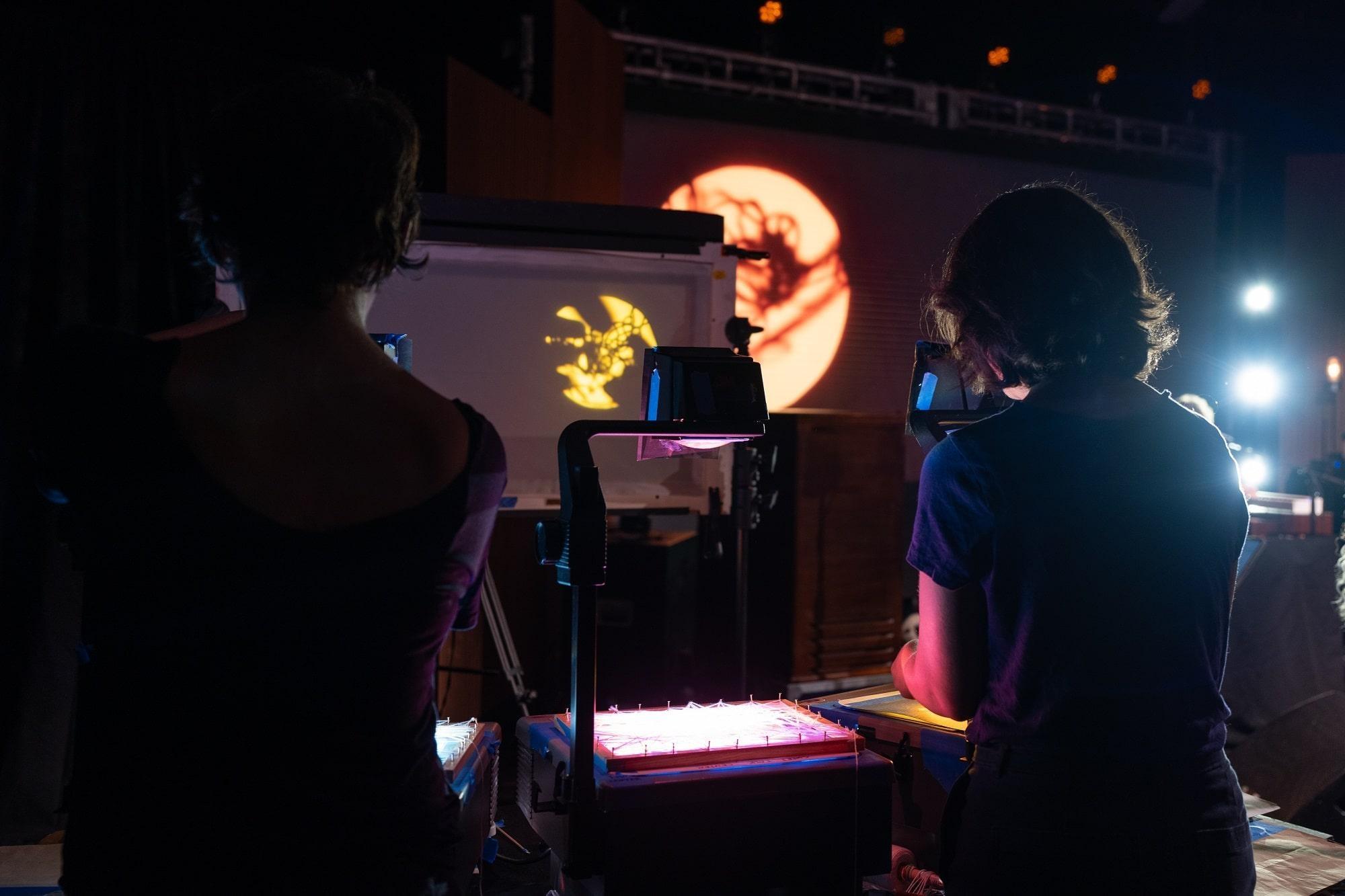 Members of Manual Cinema working an image projector for Iron & Wine's puppeteer backgroud.