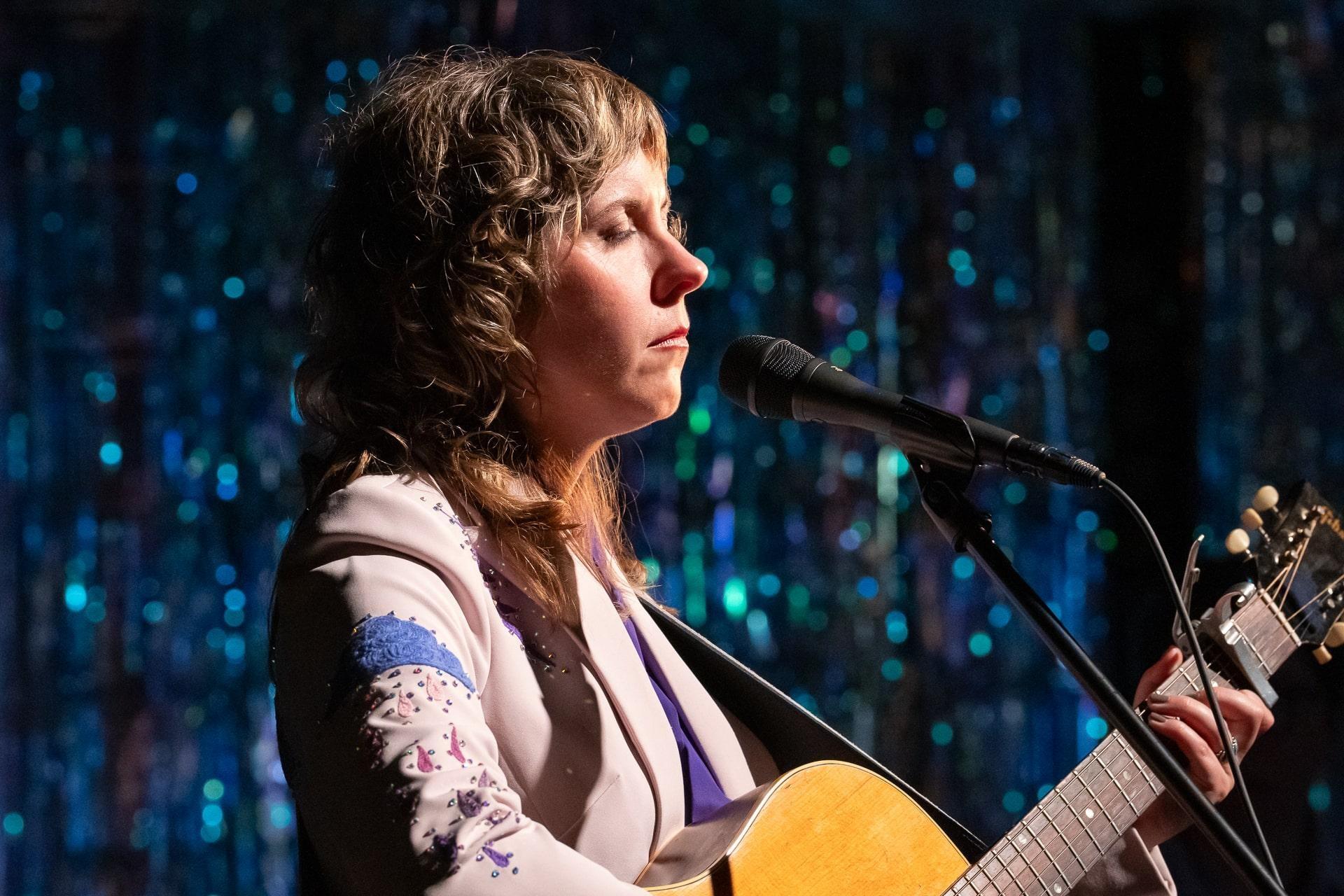 Steph Stewart of Blue Cactus playing acoustic guitar and singing into a microphone.