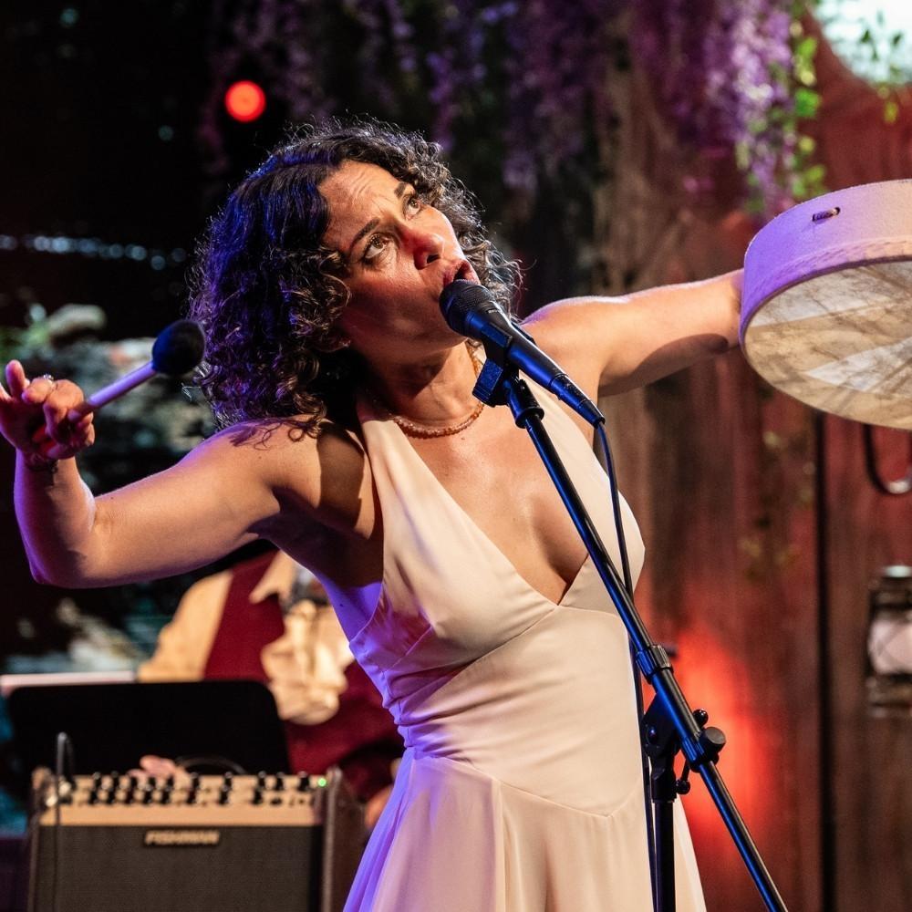Charly Lowry singing while playing a drum.